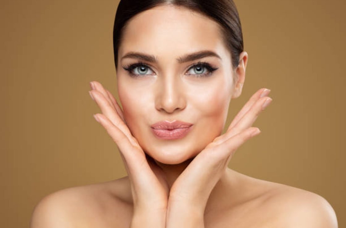 Beauty Model showing Cheekbones and Full Lips. Beautiful Woman Face Skin Care. Women Dermal Filler and Permanent Make up Cosmetology. Lip Augmentation Facial Lifting Spa Massage over Beige Background